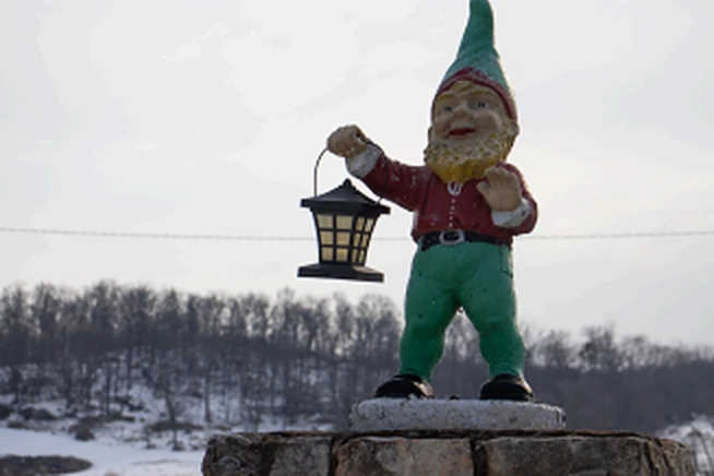 Photograph of a garden gnome holding a lantern on a stone wall in winter